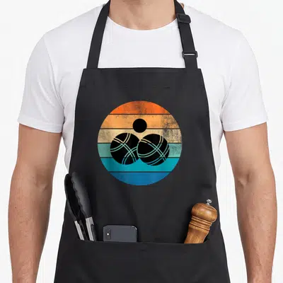 Tablier de cuisine noir avec illustration circulaire rétro de deux boules de pétanque noires sur fond de bandes colorées orange et bleues.