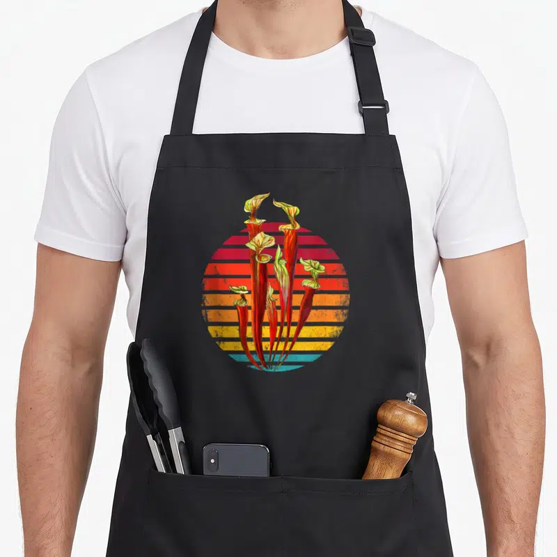 Tablier de cuisine noir avec illustration de Sarracenia sur fond de Coucher de Soleil rétro aux bandes horizontales colorées.