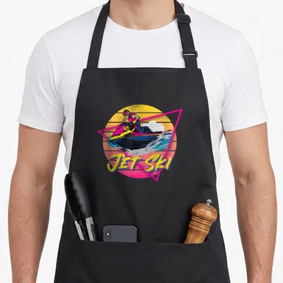 Tablier de cuisine noir avec illustration colorée d'un pilote de Jet Ski sur fond de soleil couchant et triangle géométrique rose.