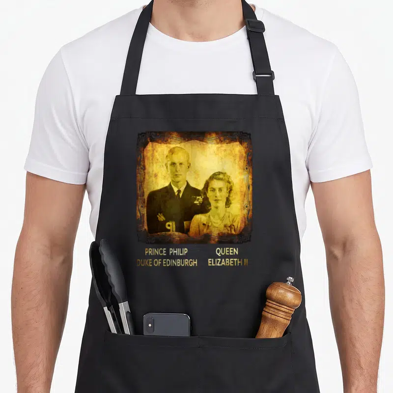 Tablier de cuisine noir avec portrait vintage de la Reine Elizabeth II et du Prince Philip, Duke of Edinburgh, encadré de motifs ornementaux.