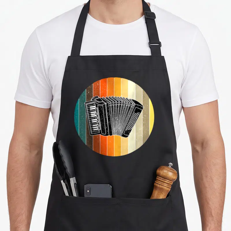Tablier de cuisine noir avec illustration circulaire d'un accordéon styrien sur fond de bandes colorées vertes, oranges et jaunes.