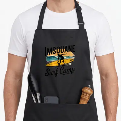 Tablier de cuisine noir avec illustration rétro d'un surfeur et du texte Imsouane Surf Camp.