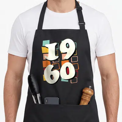 Tablier de cuisine noir avec grand motif 1960 et formes géométriques colorées sur fond gris uni.