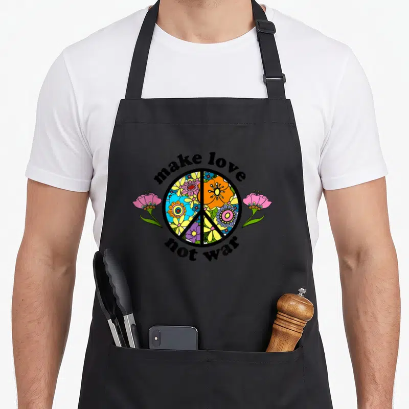 Tablier de cuisine noir avec un grand signe de la paix floral et l'inscription make love not war en typographie arrondie noire.