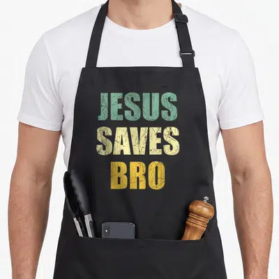 Tablier de cuisine noir avec l'inscription JESUS SAVES BRO en typographie vintage colorée et texturée.