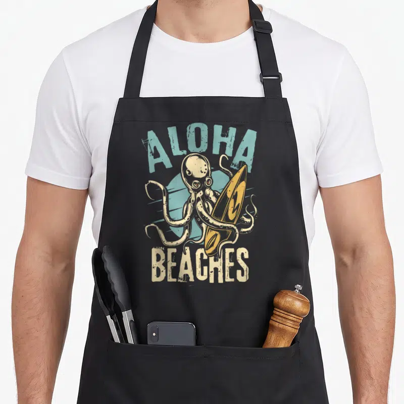 Tablier de cuisine noir avec un octopus surfeur tenant une planche et le texte Aloha Beaches en lettres délavées.