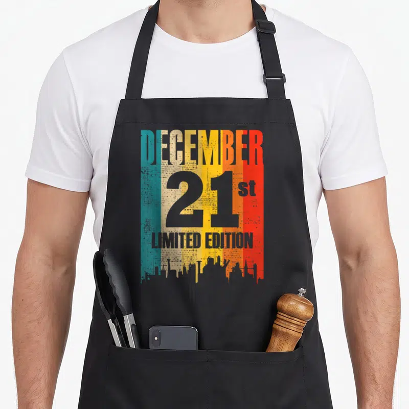 Tablier de cuisine noir avec inscription Décembre 21 sur fond de bandes colorées et skyline urbain.