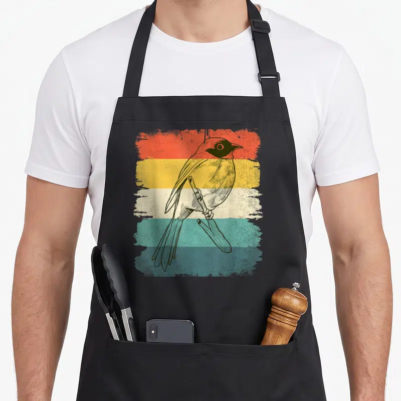 Tablier de cuisine noir avec illustration colorée d'un oiseau sur fond de bandes horizontales texturées orange jaune et bleu.