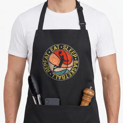 Tablier de cuisine noir avec un logo circulaire retro représentant un joueur de basket en silhouette sur une balle colorée.