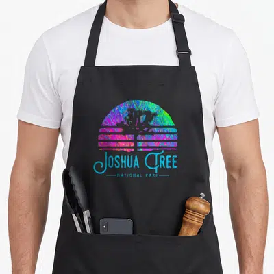 Tablier de cuisine noir avec illustration colorée style rétro représentant un coucher de soleil et le texte Joshua Tree National Park