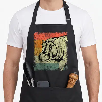 Tablier de cuisine noir avec illustration vintage d'un hippopotame sur fond de bandes colorées délavées.