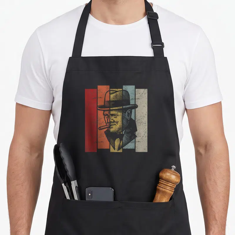 Tablier de cuisine noir avec portrait stylisé de Winston Churchill au chapeau et cigare sur fond de bandes colorées verticales.