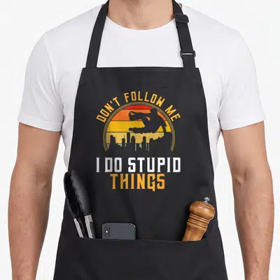 Tablier de cuisine noir avec inscription Ne me suis pas je fais des choses stupides et silhouette de saut urbain sur fond orange.