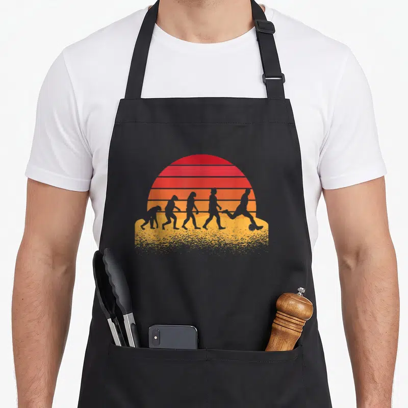 Tablier de cuisine noir avec silhouette évolutive devenant footballeur sur fond de soleil rayé orange et rouge.