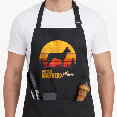 Tablier de cuisine noir avec silhouette de berger hollandais et texte Dutch Shepherd Mom sur fond de soleil retro.