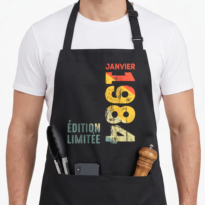 Tablier de cuisine noir avec inscription verticale « Édition limitée » Janvier 1984 en typographie rétro colorée.