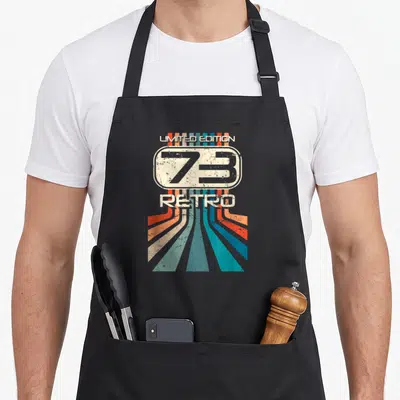 Tablier de cuisine noir avec un motif rétro affichant Limited Edition 73 Retro et des rayons colorés.
