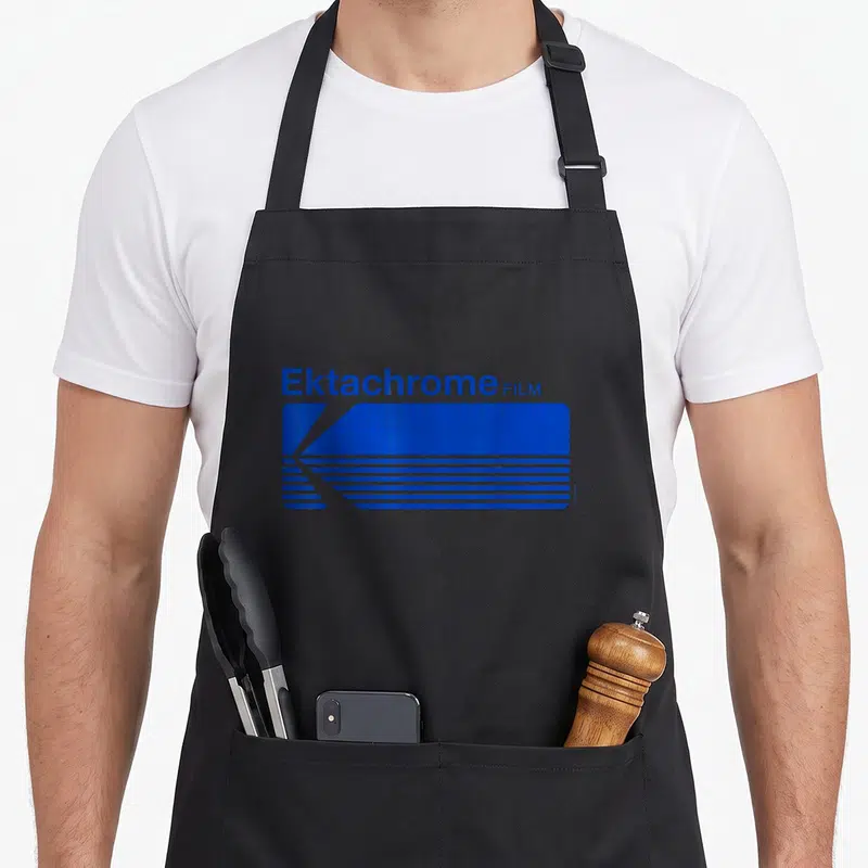 Tablier de cuisine noir avec le logo Ektachrome Film en bleu et des lignes horizontales géométriques.