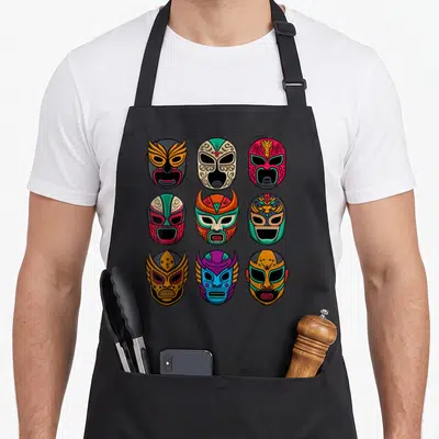 Tablier de cuisine noir avec neuf masques de luchadores colorés disposés en grille sur le devant.