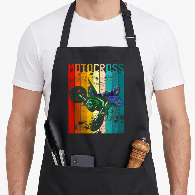 Tablier de cuisine noir avec illustration d'une moto de motocross verte et le texte MOTOCROSS en bandes colorées rétro.