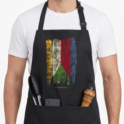 Tablier de cuisine noir avec drapeau Comores vintage aux couleurs usées et texte COMOROS en bas.