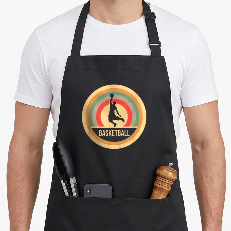 Tablier de cuisine noir avec logo circulaire rétro montrant un joueur de basket en silhouette et le mot BASKETBALL.