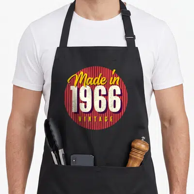 Tablier de cuisine noir avec emblème circulaire rouge et texte « Made in 1966 Vintage » en jaune et blanc.