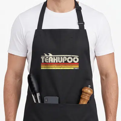 Tablier de cuisine noir avec logo Teahupoo Tahiti et planche de surf stylisée sur fond de rayures colorées dégradées.