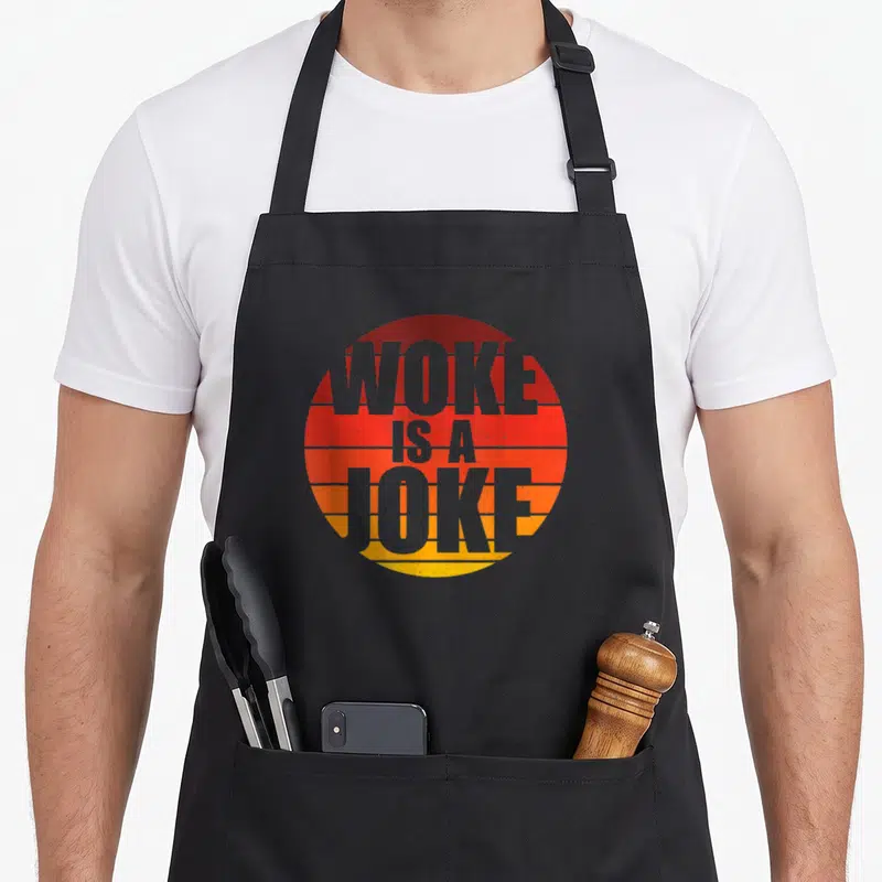 Tablier de cuisine noir avec un motif circulaire orange et jaune portant l'inscription Woke Is A Joke en lettres grises.