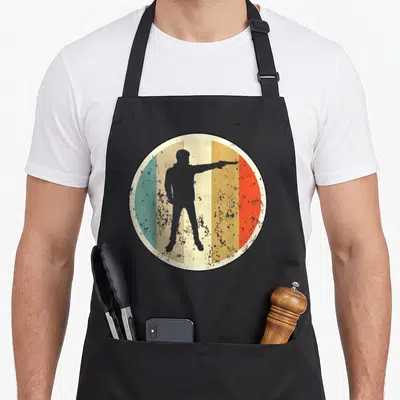 Tablier de cuisine noir avec silhouette de tireur au pistolet sur fond circulaire rétro multicolore.