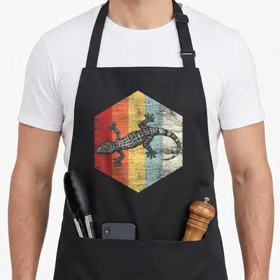 Tablier de cuisine noir avec illustration d'un lézard sur un hexagone aux bandes colorées rouges, oranges, jaunes et bleues.
