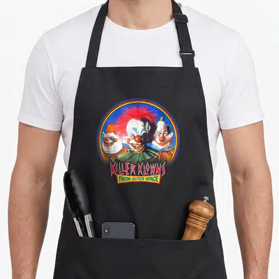 Tablier de cuisine noir avec illustration circulaire de trois clowns aux cheveux colorés et texte Killer Klowns From Outer Space en bas.