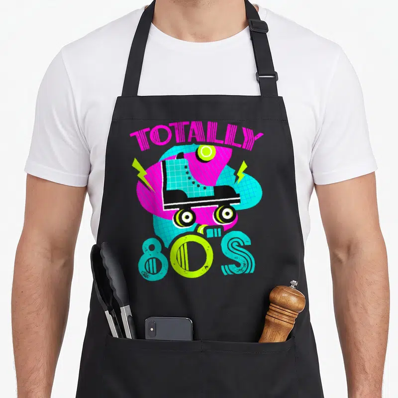 Tablier de cuisine noir avec une patinette rose et le texte Totally 80s en lettres colorées.