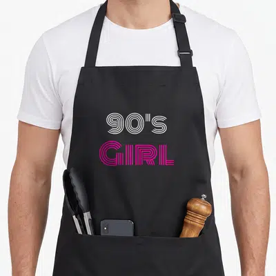 Tablier de cuisine noir avec l'inscription 90's Girl en lettres rayées blanches et roses vives sur fond uni.