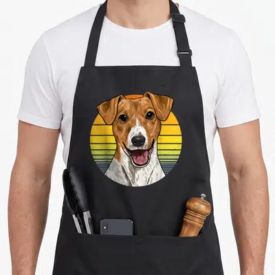Tablier de cuisine noir avec illustration circulaire d'un Jack Russel Terrier sur fond de coucher de soleil rétro jaune et bleu.