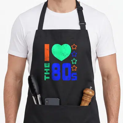 Tablier de cuisine noir avec le texte I Love The 80s, un grand cœur vert et quatre étoiles colorées sur le devant.