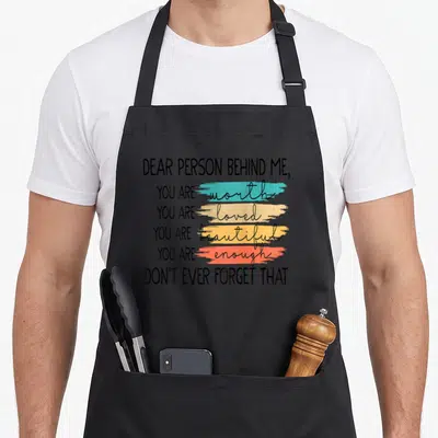 Tablier de cuisine noir avec inscription rétro « Dear Person Behind Me » et touches de couleur turquoise, beige, orange et rouge.
