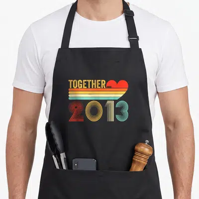 Tablier de cuisine noir avec motif rétro Together Since 2013 et cœur coloré aux lignes horizontales.