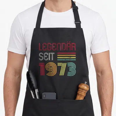 Tablier de cuisine noir avec inscription Légendaire Seit 1973 en lettres colorées style années septante.