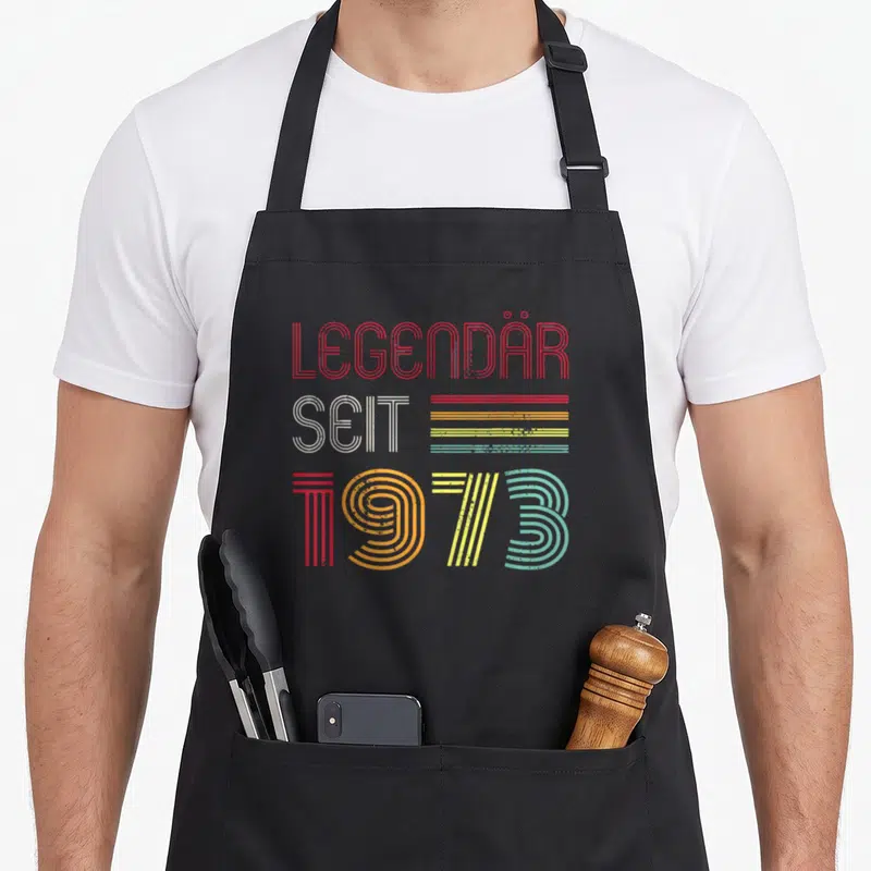 Tablier de cuisine noir avec inscription Légendaire Seit 1973 en lettres colorées style années septante.