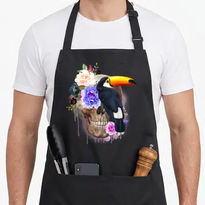 Tablier de cuisine noir avec illustration crâne, toucan et fleurs aquarelle vintage.