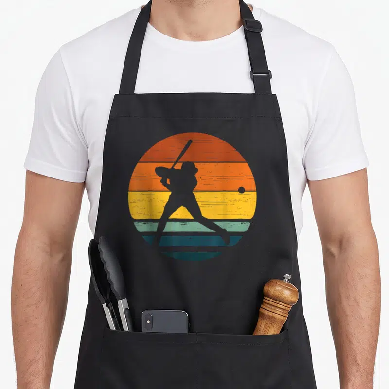 Tablier de cuisine noir avec silhouette de softballeuse sur fond de soleil couchant aux bandes orange jaune et bleu.