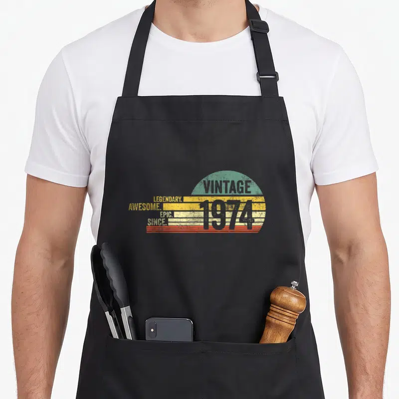 Tablier de cuisine noir avec un motif rétro 1974 aux couleurs pastel et texte blanc.