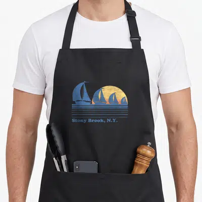 Tablier de cuisine noir avec illustration de voiliers bleus devant un soleil couchant jaune et l'inscription Stony Brook, N.Y.