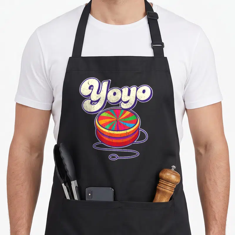 Tablier de cuisine noir avec illustration colorée d'un yoyo rétro et le mot Yoyo en lettres capitales blanches à contour violet.