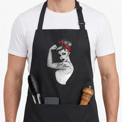 Tablier de cuisine noir avec illustration d'une femme aux cheveux en chignon portant un bandeau rouge et le texte Girl Power sur son bras.