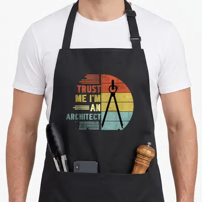 Tablier de cuisine noir avec inscription Trust Me I'm An Architect et boussole rétro sur fond coloré segmenté.