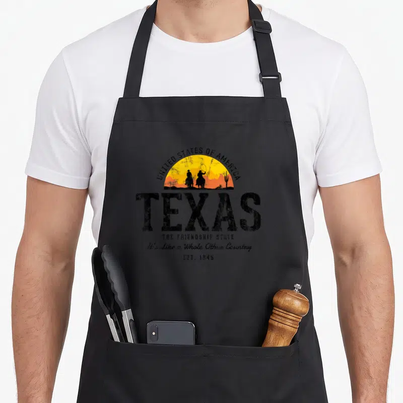 Tablier de cuisine noir avec illustration rétro Texas cow-boys et texteUnited States of America en arc de cercle.
