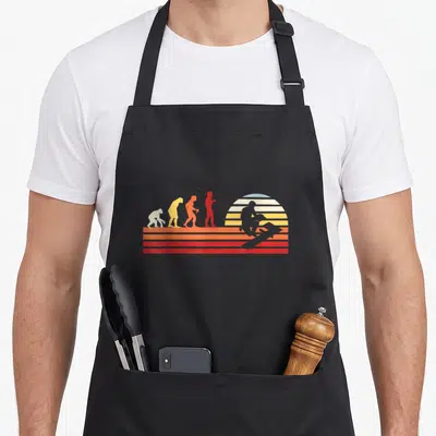 Tablier de cuisine noir avec illustration retro montrant l'évolution humaine vers un carreleur assis sur fond de soleil couchant strié.