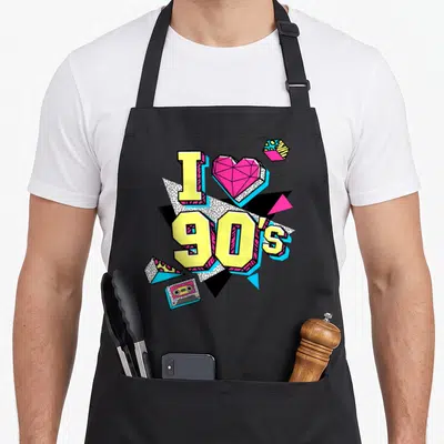 Tablier de cuisine noir avec inscription I love 90's, cœur rose géométrique et cassette audio colorée sur fond graphique.